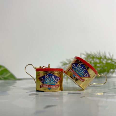 Mini gold Blue Diamond canned almond earrings on a white and speckled stone backdrop with faux plants.