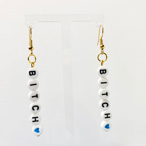 Hanging earrings with white beads with black letters spelling bitch with a heart bead. 