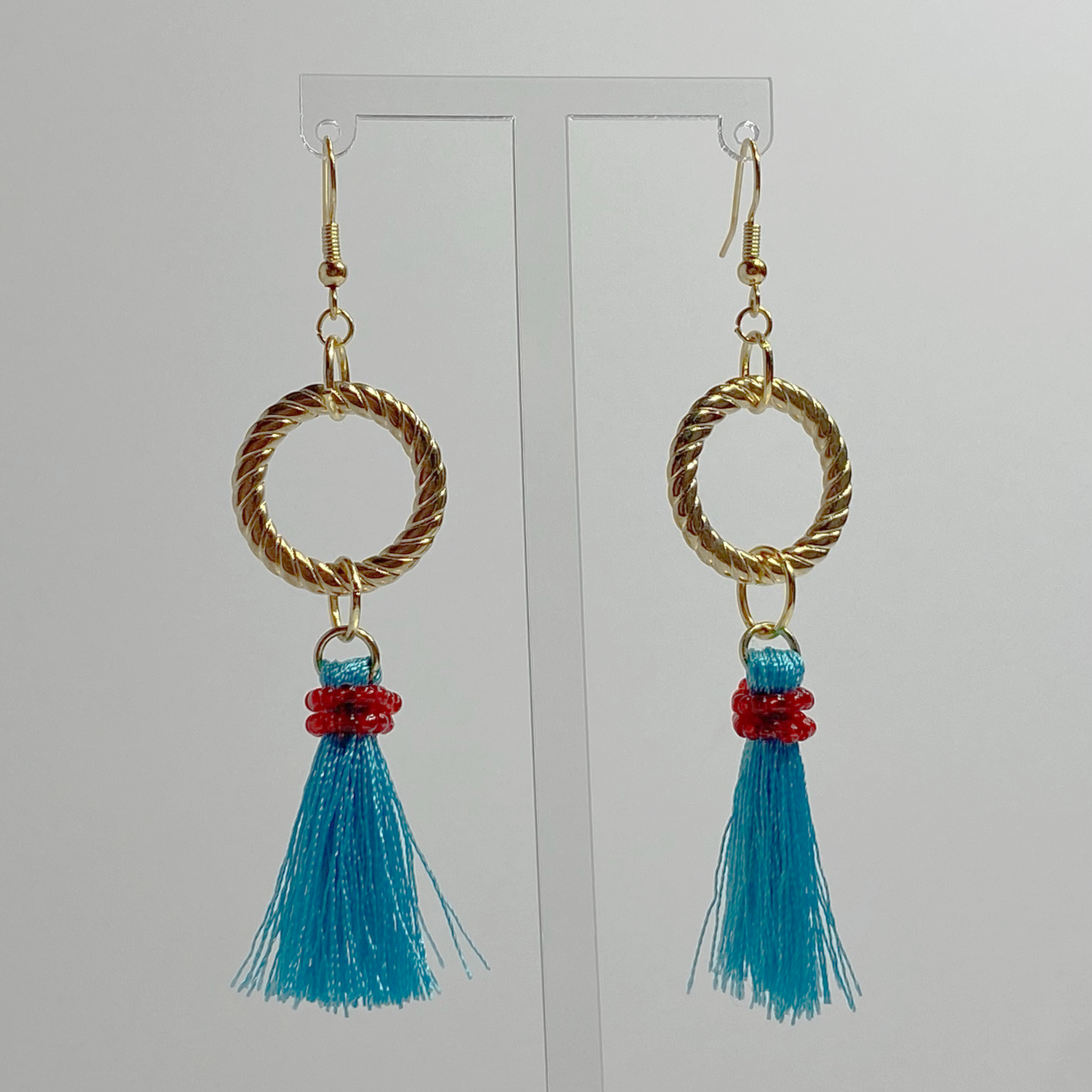 Gold-toned hanging earrings with a gold-plated hoop with hanging blue tassels with red beads. 