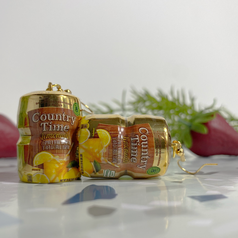 Mini gold Country Time lemonade mix earrings on a speckled stone backdrop with faux strawberries. 