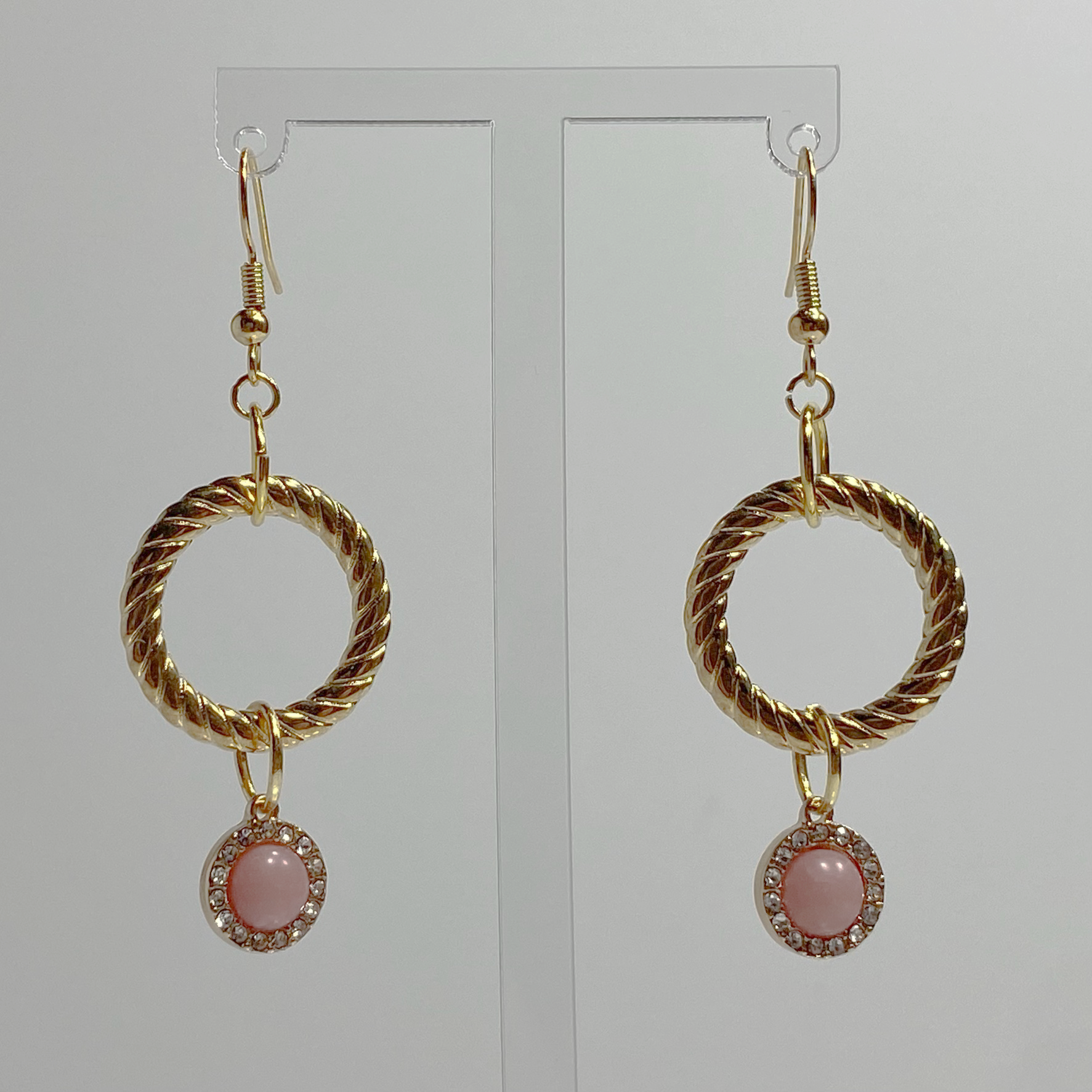 Gold-toned hanging earrings with a gold-plated hoop with a small with a hanging pink gem surrounded by white crystals.